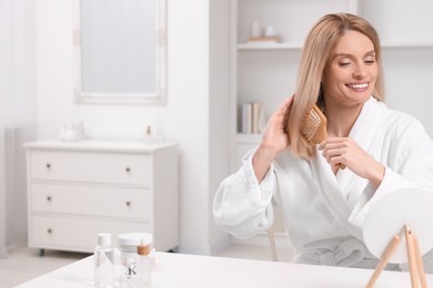 Photo of Beautiful happy woman brushing her hair at white table in room, space for text
