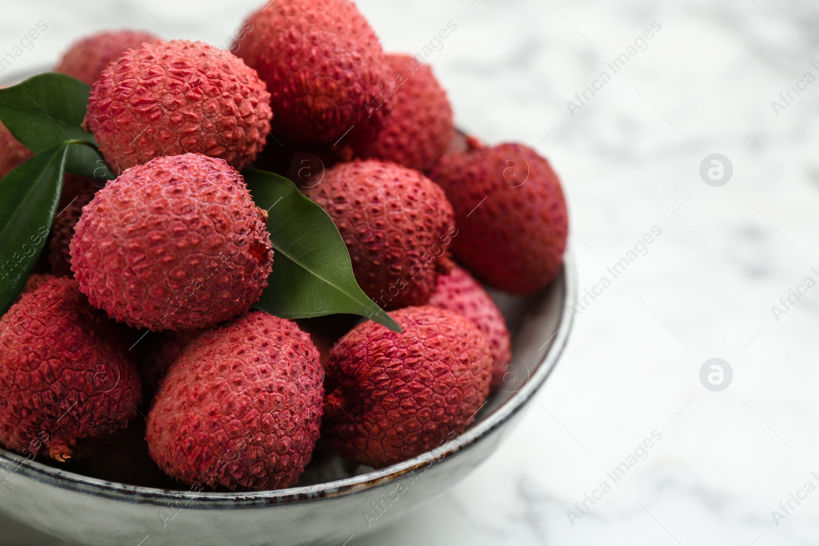 Photo of Fresh ripe lychee fruits in ceramic bowl on white table, closeup. Space for text