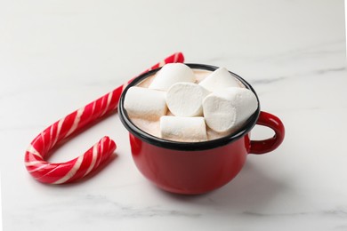 Photo of Tasty hot chocolate with marshmallows and candy cane on white marble table, closeup