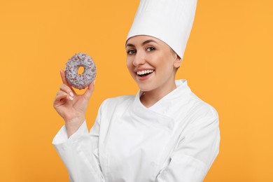 Photo of Happy professional confectioner in uniform holding delicious doughnut on yellow background