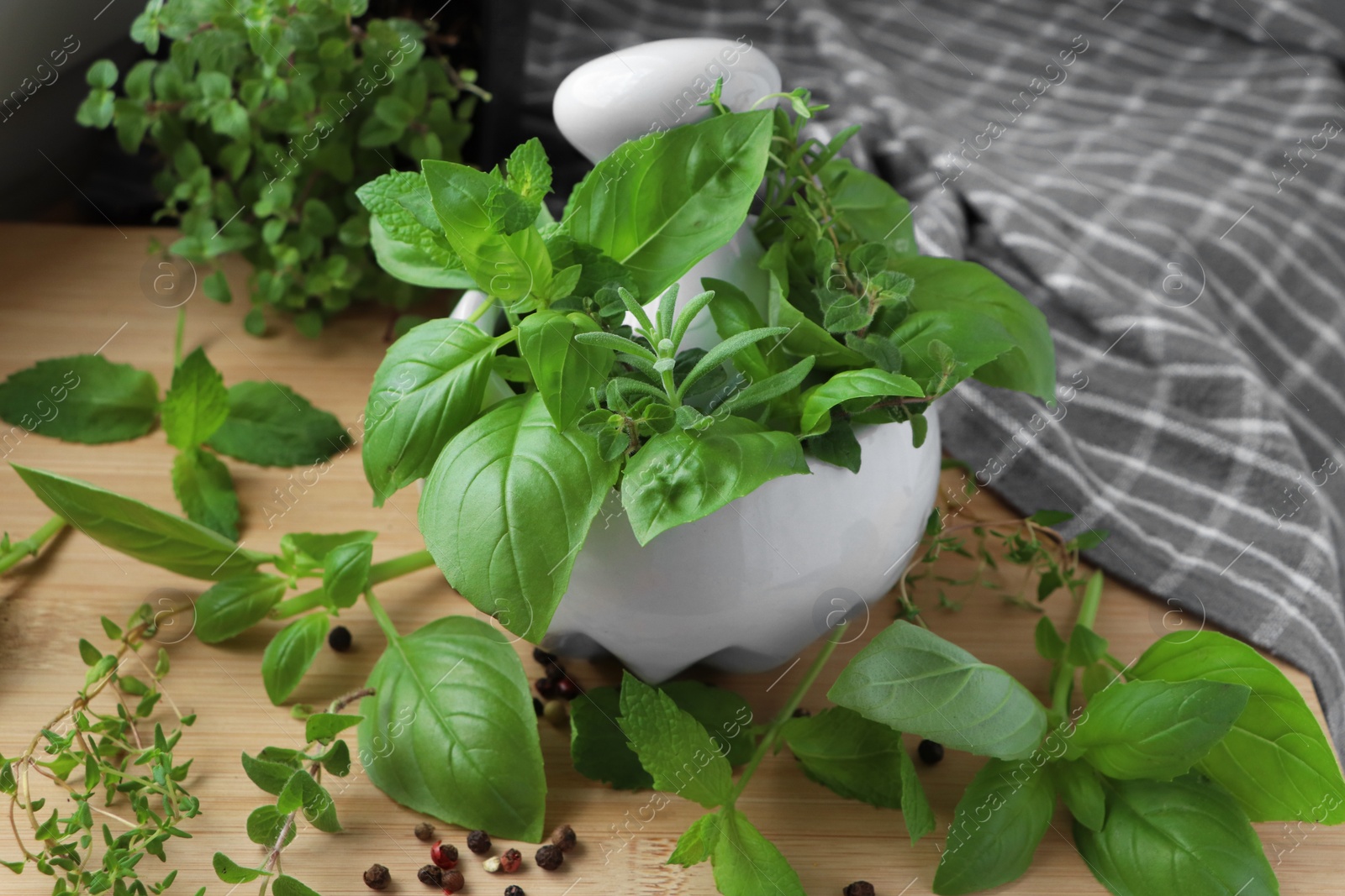 Photo of Mortar with different fresh herbs and black peppercorns on wooden table, closeup