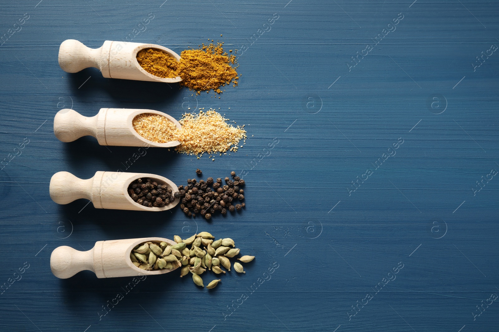 Photo of Wooden scoops with different spices on blue table, flat lay. Space for text