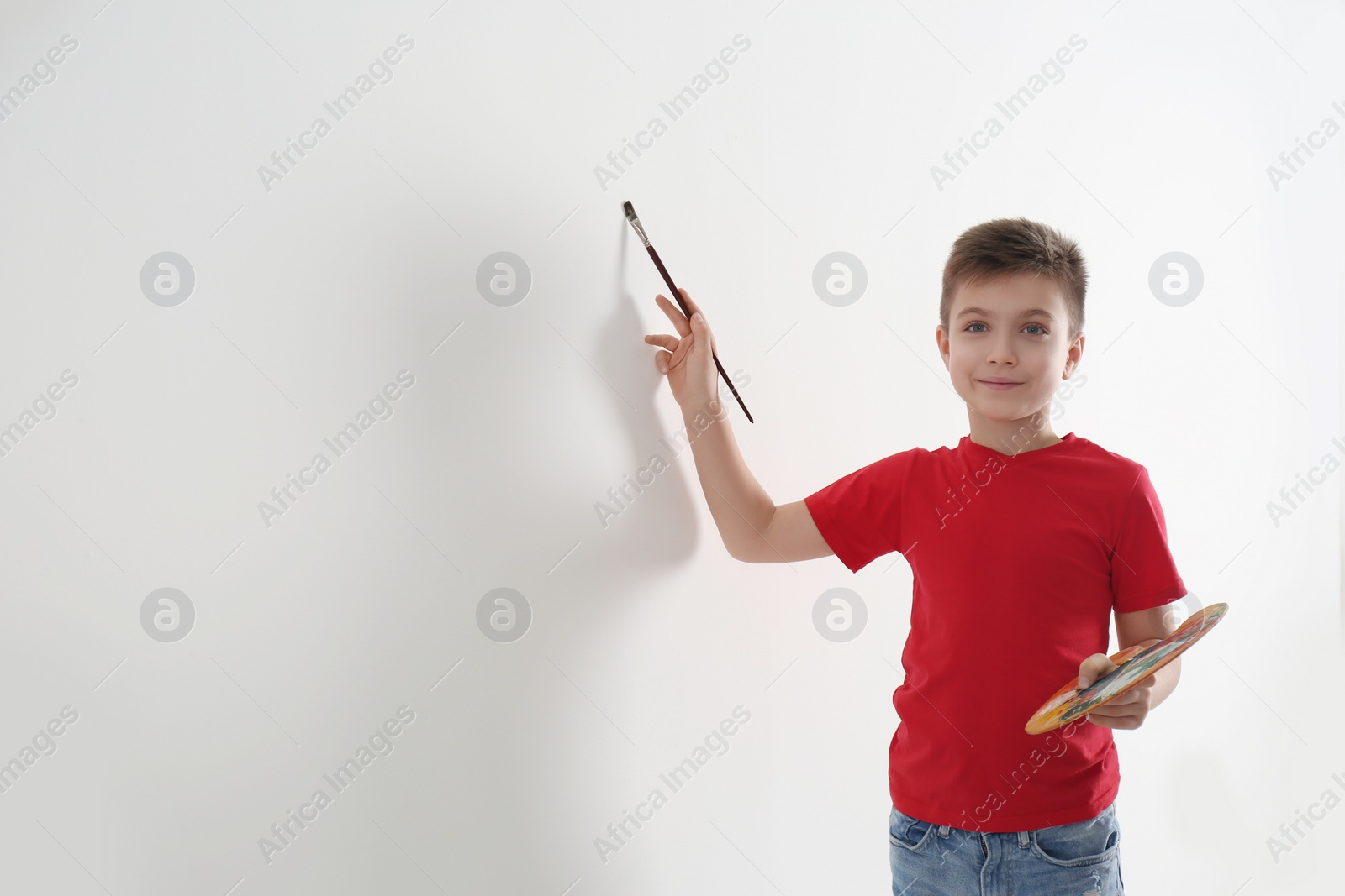 Photo of Little child painting on blank white wall indoors, space for text