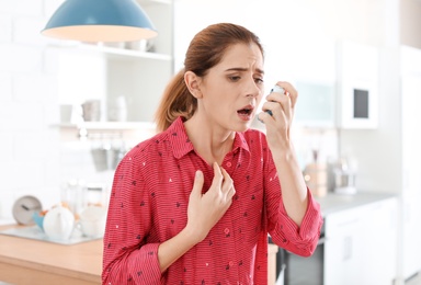 Photo of Young woman using asthma inhaler in kitchen