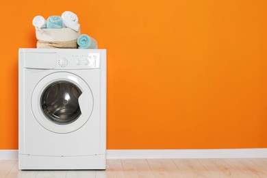 Washing machine with clean towels near orange wall indoors, space for text. Interior design