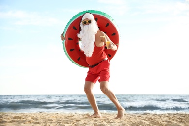 Photo of Santa Claus with cocktail and inflatable ring on beach. Christmas vacation