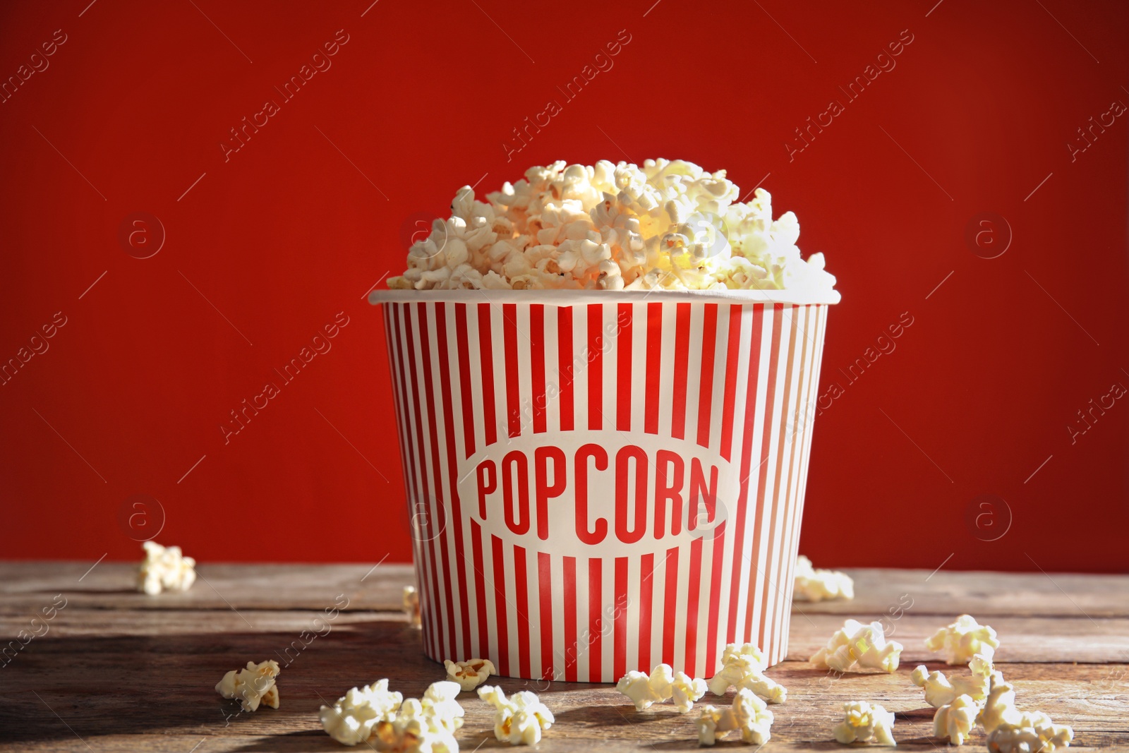 Photo of Bucket of tasty popcorn on table against red background. Watching cinema