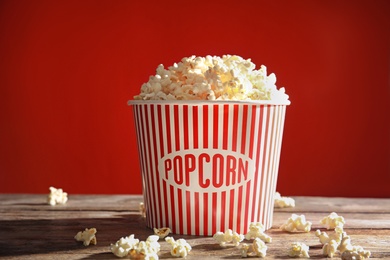 Photo of Bucket of tasty popcorn on table against red background. Watching cinema