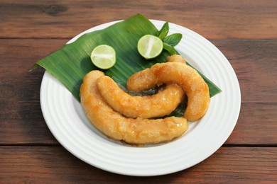 Plate with delicious fried bananas, lime and mint leaves on wooden table
