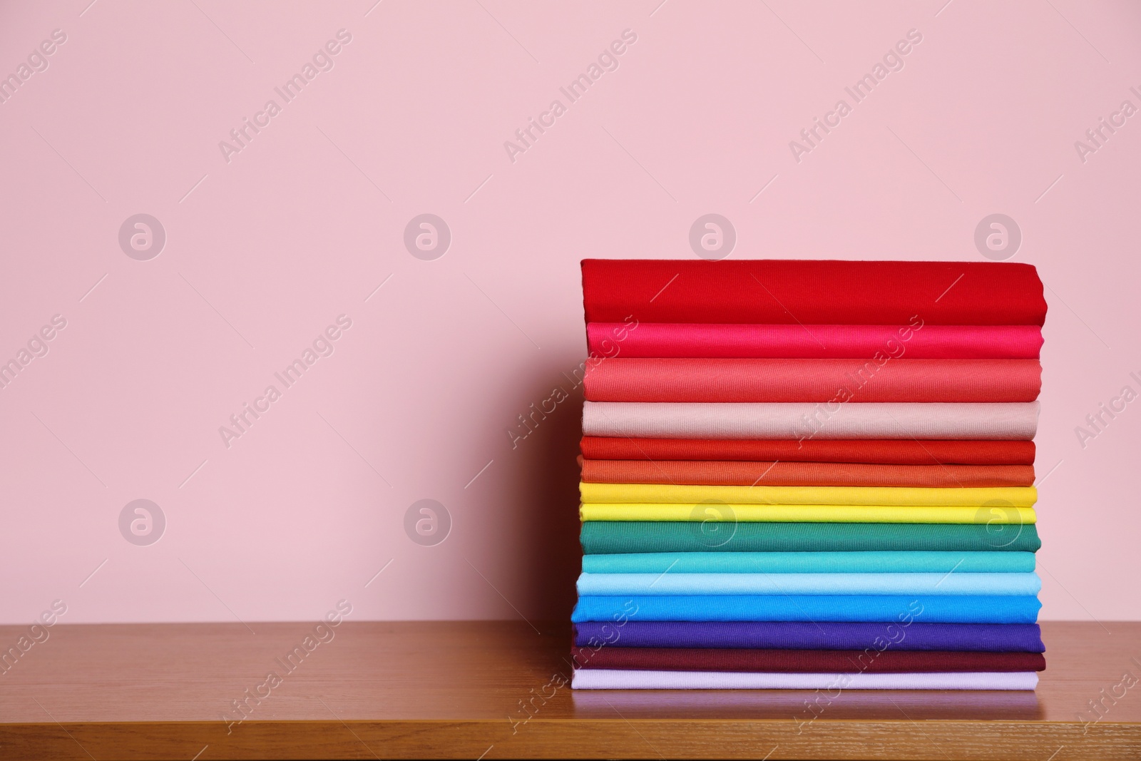 Photo of Pile of bright t-shirts on table against color background