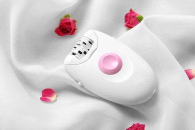 Photo of Modern epilator and flowers on light fabric