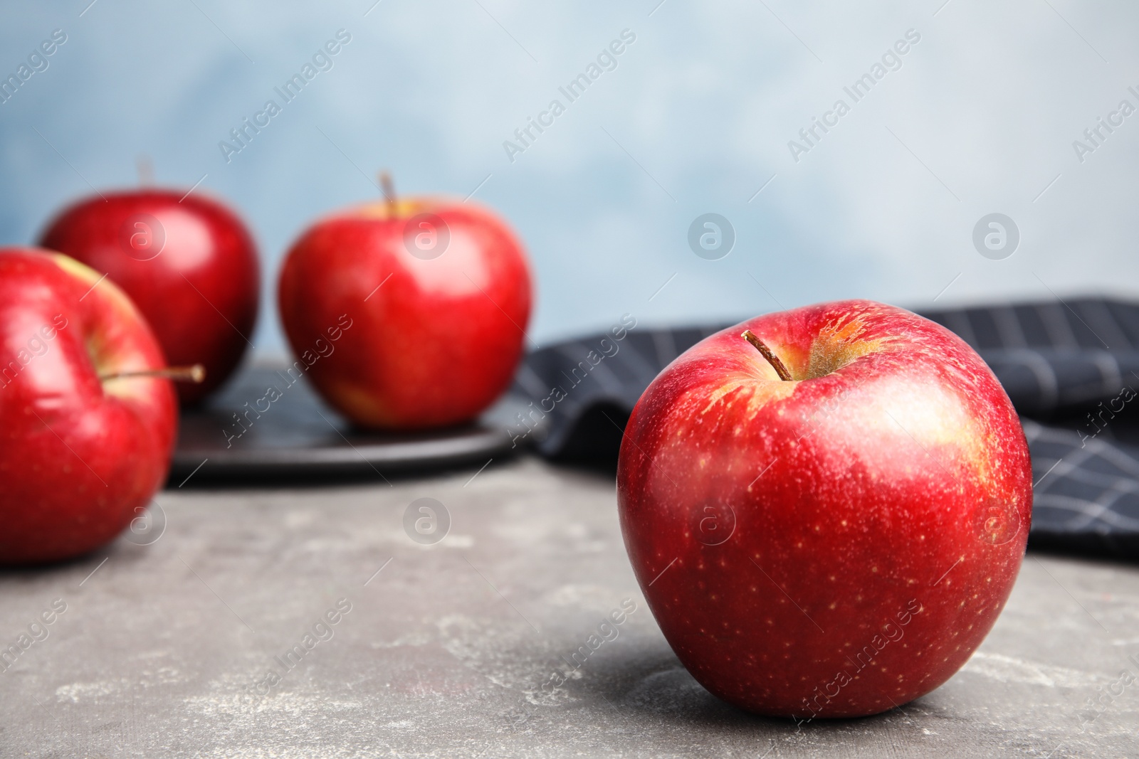 Photo of Ripe juicy red apple on grey table against blue background. Space for text