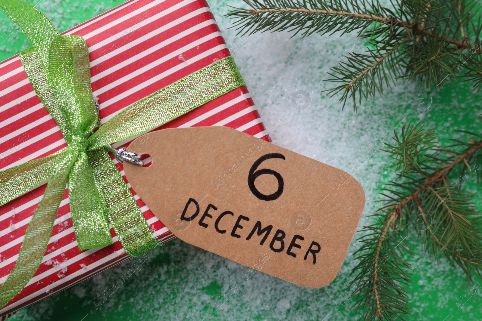 Photo of Gift box, paper tag with date 6th of December and fir tree branch on green background, flat lay. Saint Nicholas Day