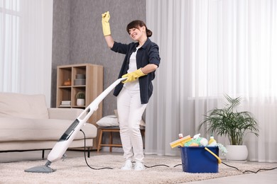 Photo of Happy young housewife having fun while cleaning carpet at home