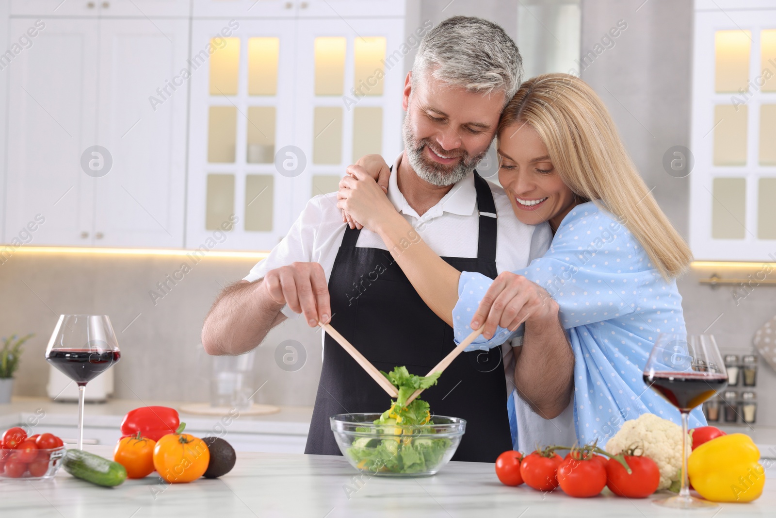 Photo of Happy affectionate couple cooking together at white table in kitchen