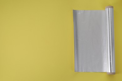 Photo of Roll of aluminum foil on yellow background, top view. Space for text
