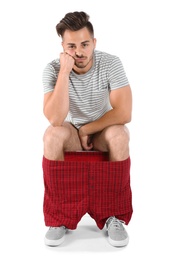 Young man sitting on toilet bowl. Isolated on white