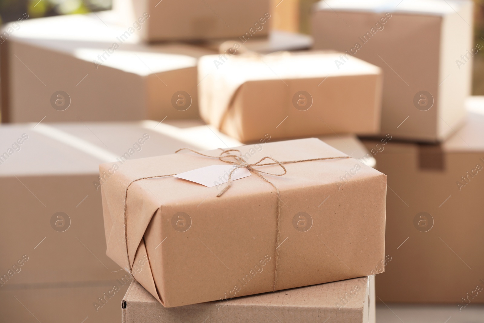 Photo of Parcel with tag and blurred stacked boxes on background, indoors