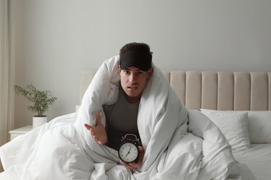 Photo of Emotional man with alarm clock in bed. Being late because of oversleeping