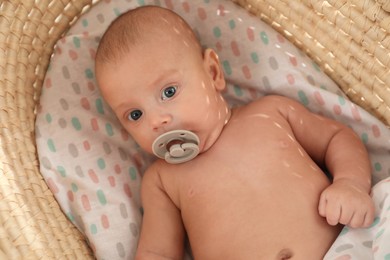 Photo of Cute little baby with pacifier lying in cradle, top view