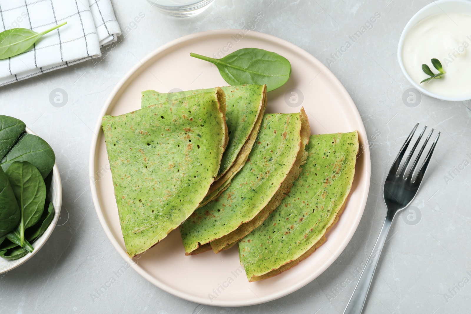 Photo of Tasty spinach crepes served on light grey marble table, flat lay