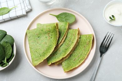 Tasty spinach crepes served on light grey marble table, flat lay