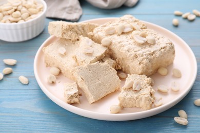 Plate with pieces of tasty halva and peanuts on light blue wooden table, closeup