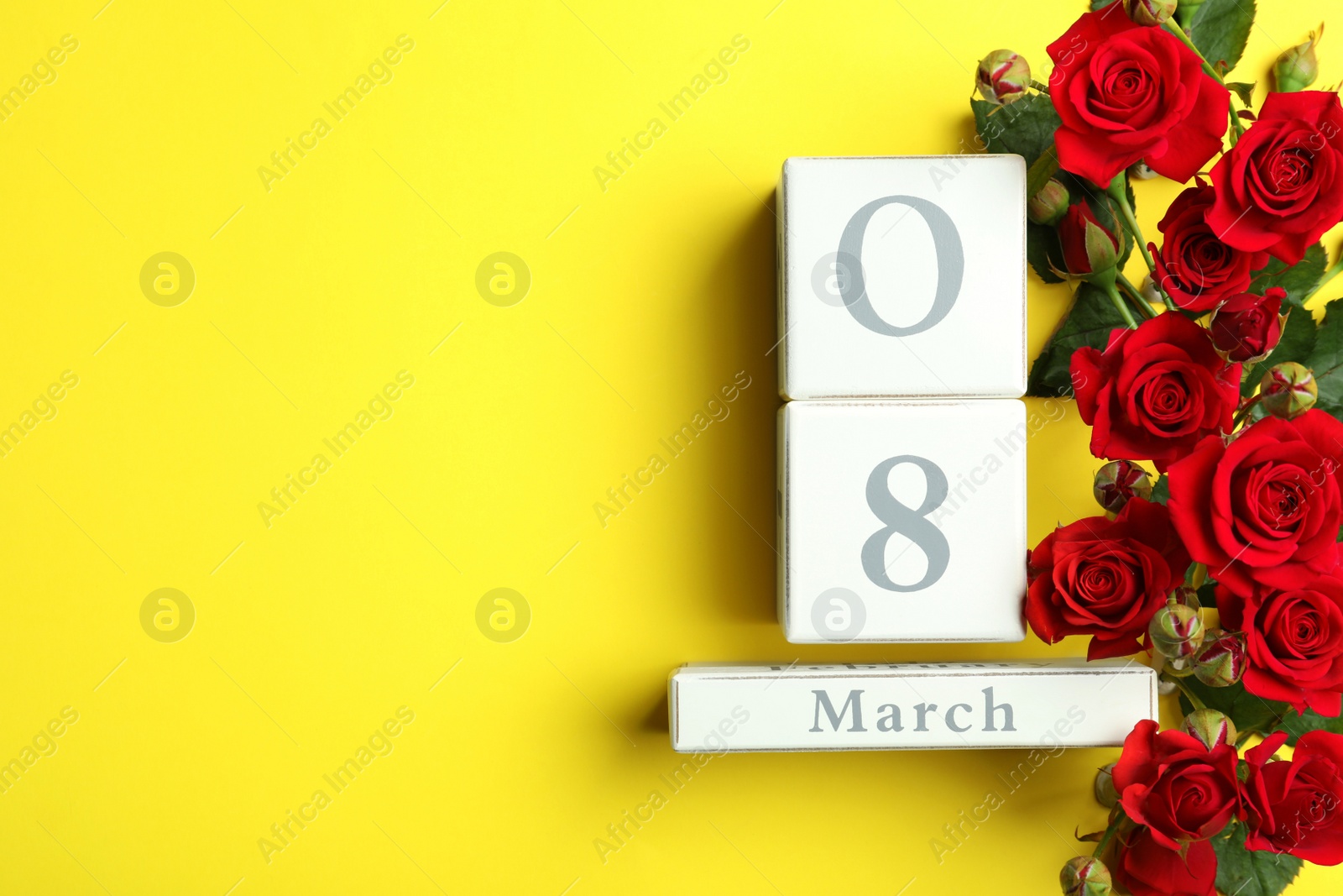 Photo of Wooden block calendar with date 8th of March and roses on yellow background, flat lay. Space for text