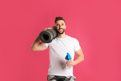 Photo of Handsome man with yoga mat and shaker on pink background