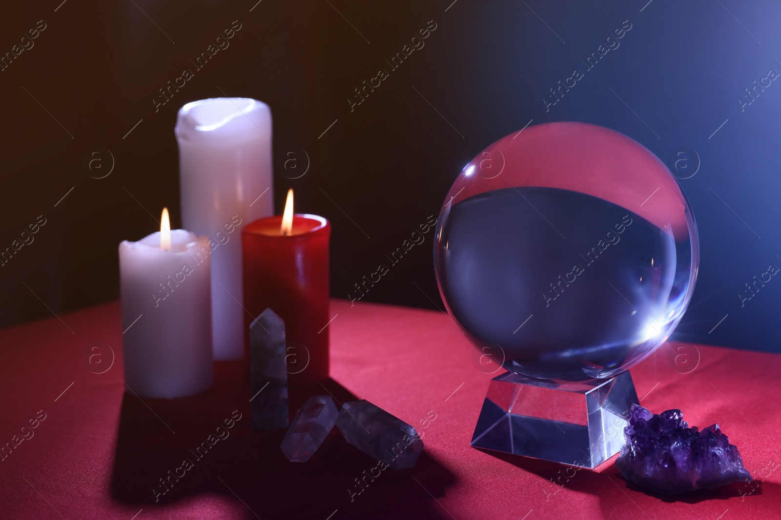 Photo of Crystal prediction ball, candles and stones on table in darkness. Fortune telling