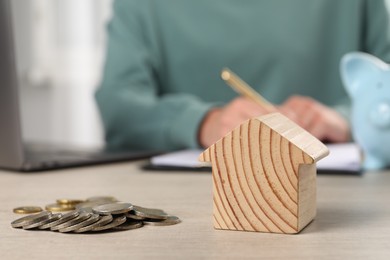 Woman planning budget at wooden table, focus on house model and coins