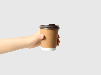 Woman holding takeaway paper coffee cup on light grey background, closeup