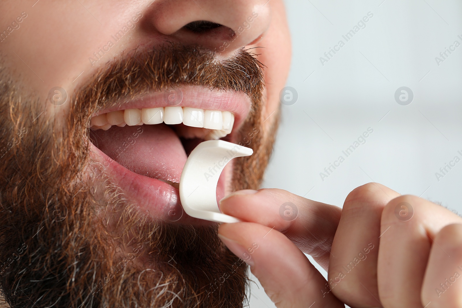 Photo of Man putting chewing gum into mouth on blurred background, closeup