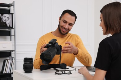 Photo of Young professional photographer showing camera to woman in modern photo studio