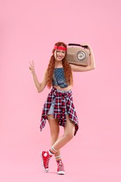 Photo of Stylish young hippie woman with radio showing V-sign on pink background