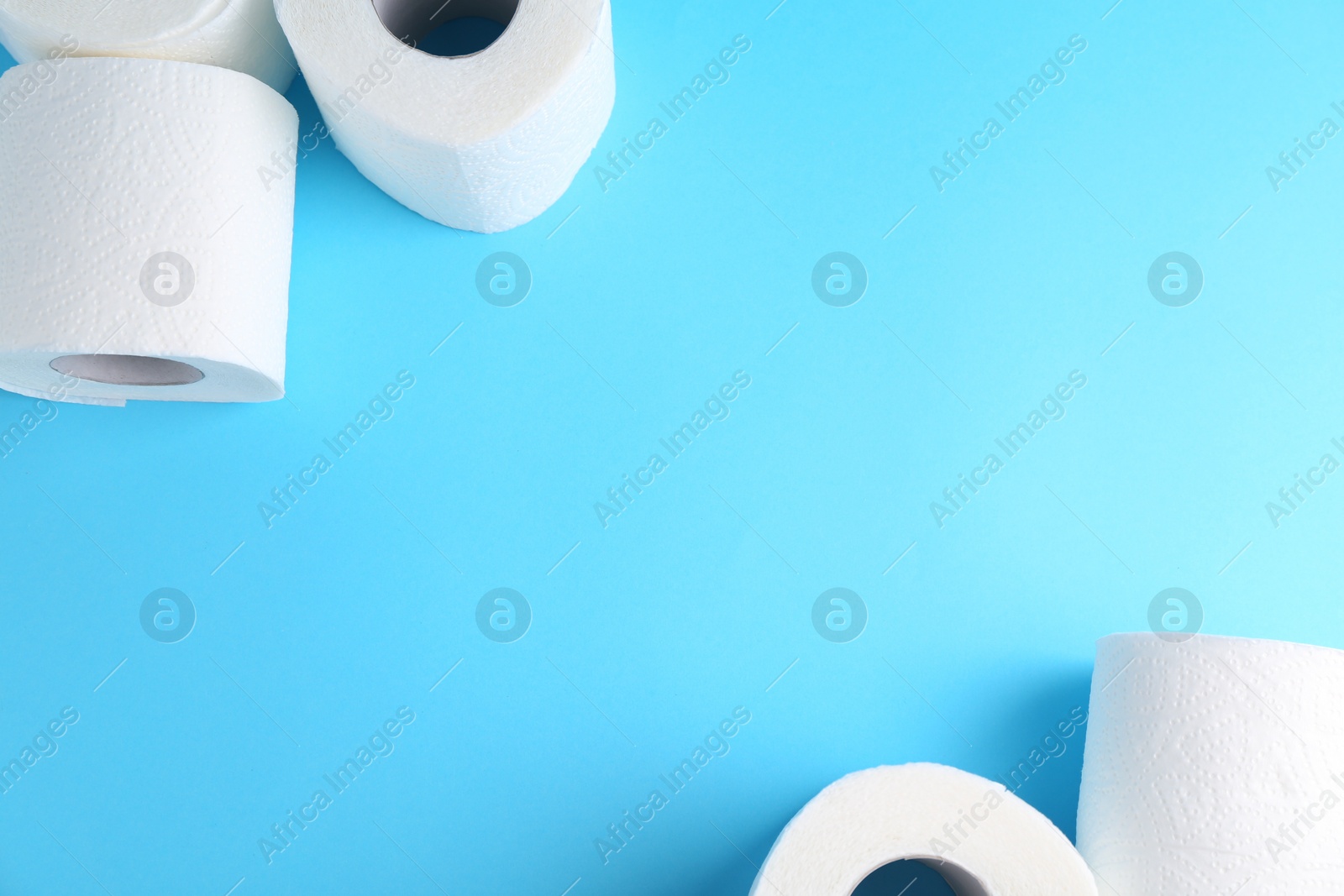 Photo of Soft toilet paper rolls on light blue background, flat lay. Space for text