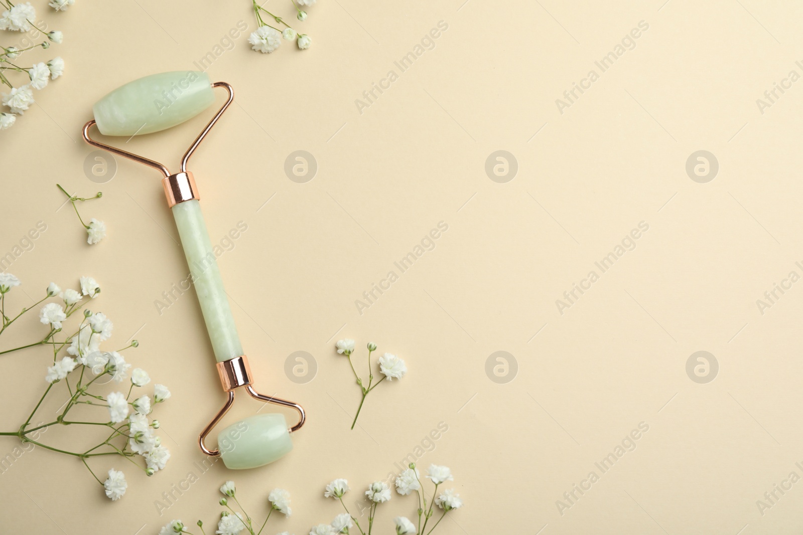 Photo of Natural face roller and flowers on beige background, flat lay. Space for text