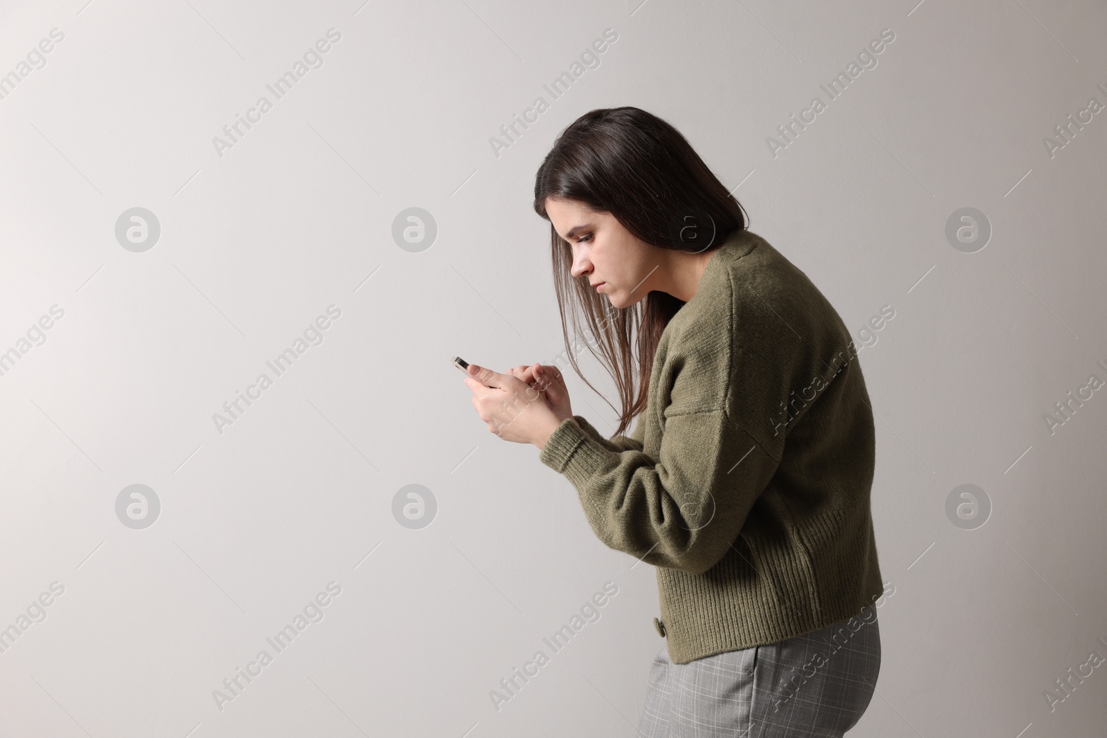 Photo of Young woman with bad posture using smartphone on grey background. Space for text