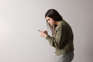 Photo of Young woman with bad posture using smartphone on grey background. Space for text