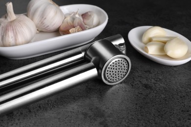Garlic press with cloves and bulbs on grey table, closeup