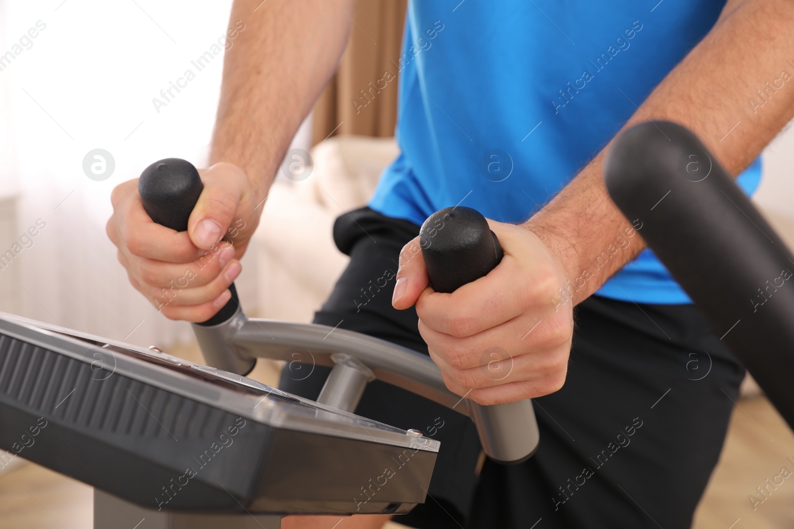 Photo of Man using modern elliptical machine indoors, closeup