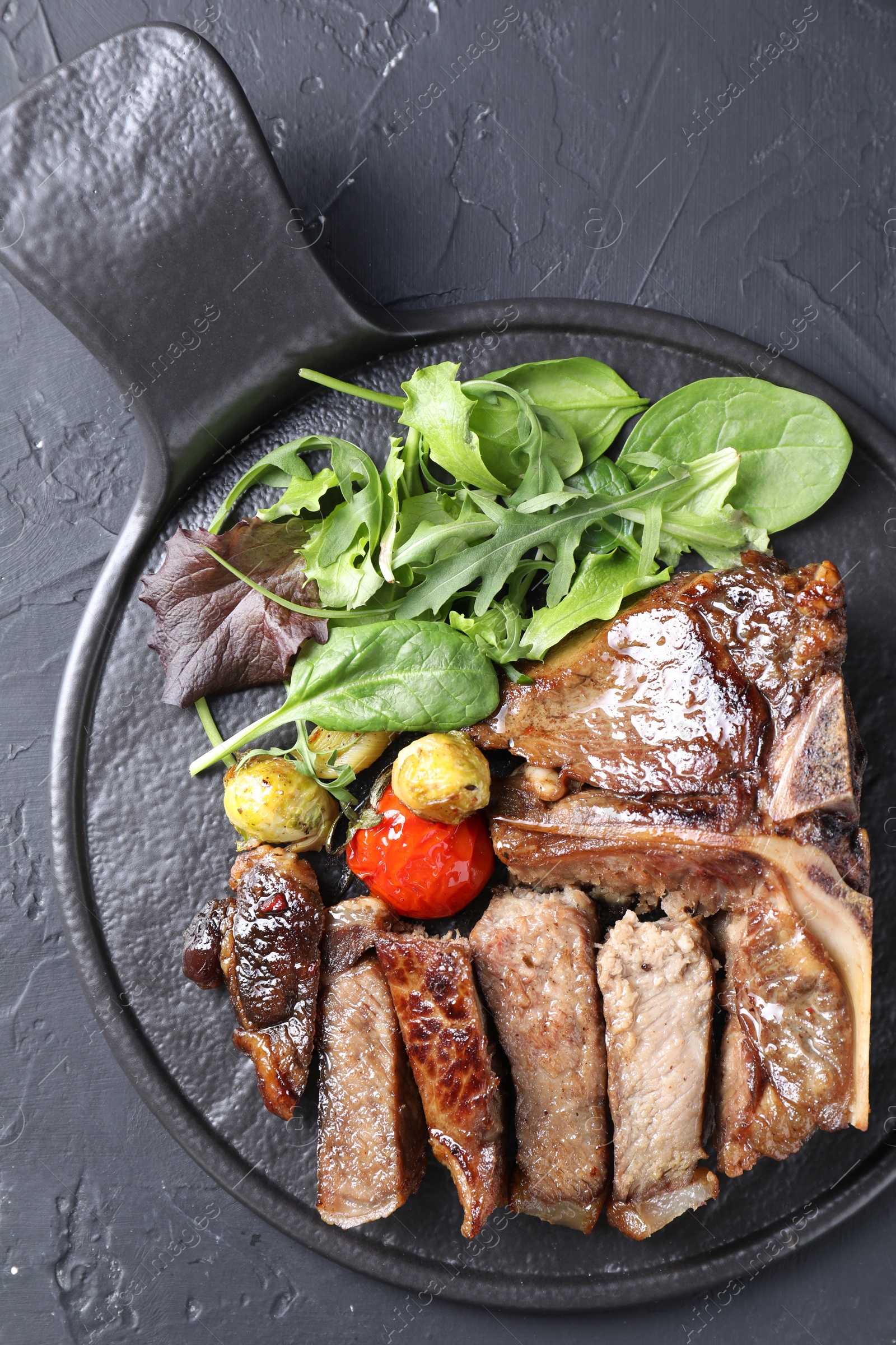 Photo of Delicious grilled beef meat, vegetables and greens on black table, top view