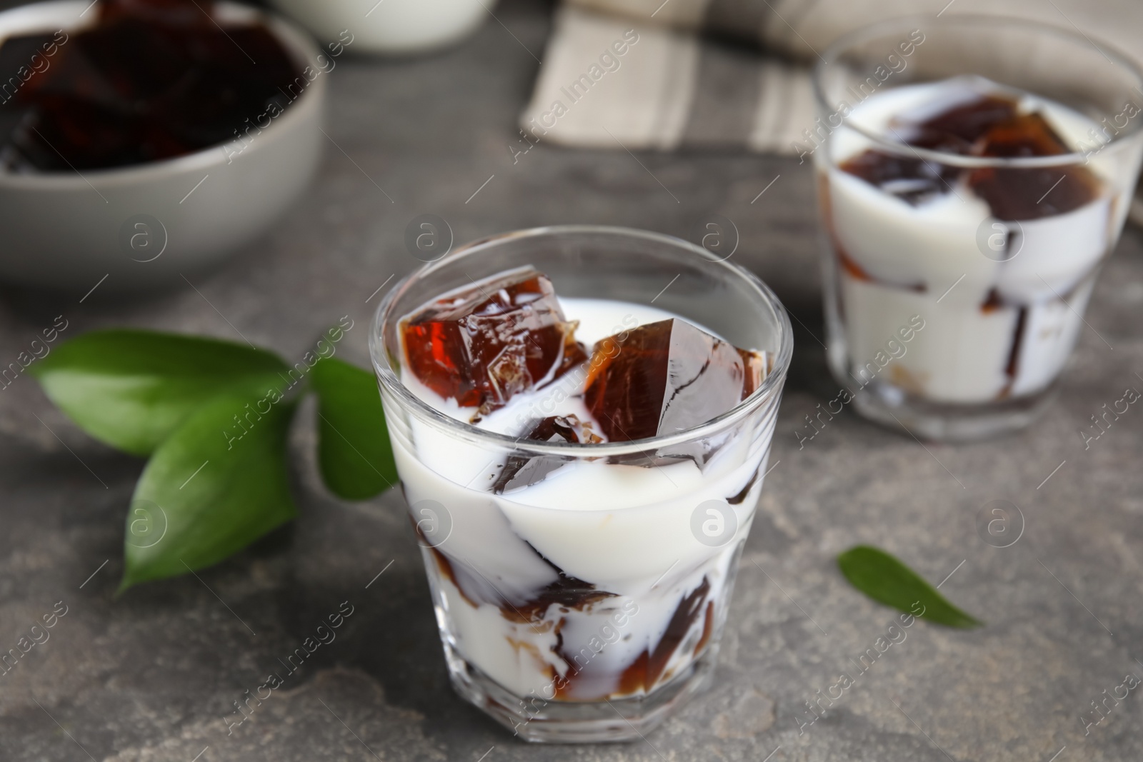 Photo of Glasses of milk with delicious grass jelly on grey table, closeup