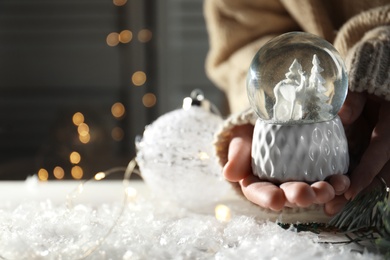 Woman holding Christmas snow globe on blurred background, closeup. Space for text