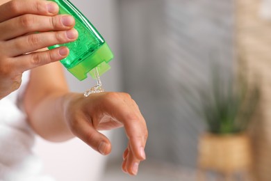 Photo of Young woman applying aloe gel onto her hand in bathroom, closeup. Space for text