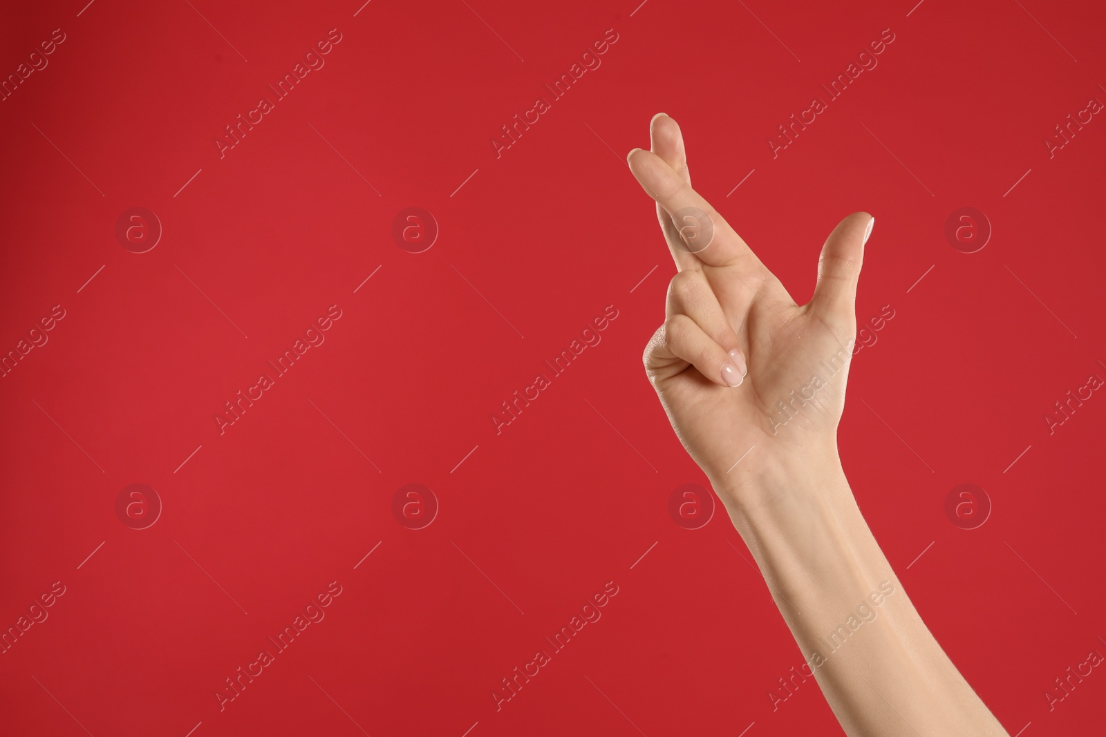 Photo of Woman with crossed fingers and space for text on red background, closeup. Superstition concept