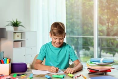 Photo of Cute boy doing homework at table with school stationery indoors