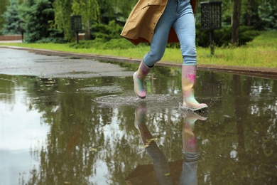 Photo of Woman with rubber boots running in puddle, closeup. Rainy weather