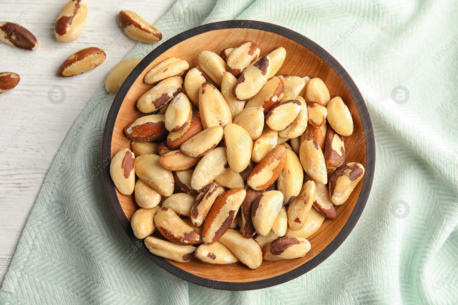 Photo of Plate with Brazil nuts and fabric on wooden table, top view