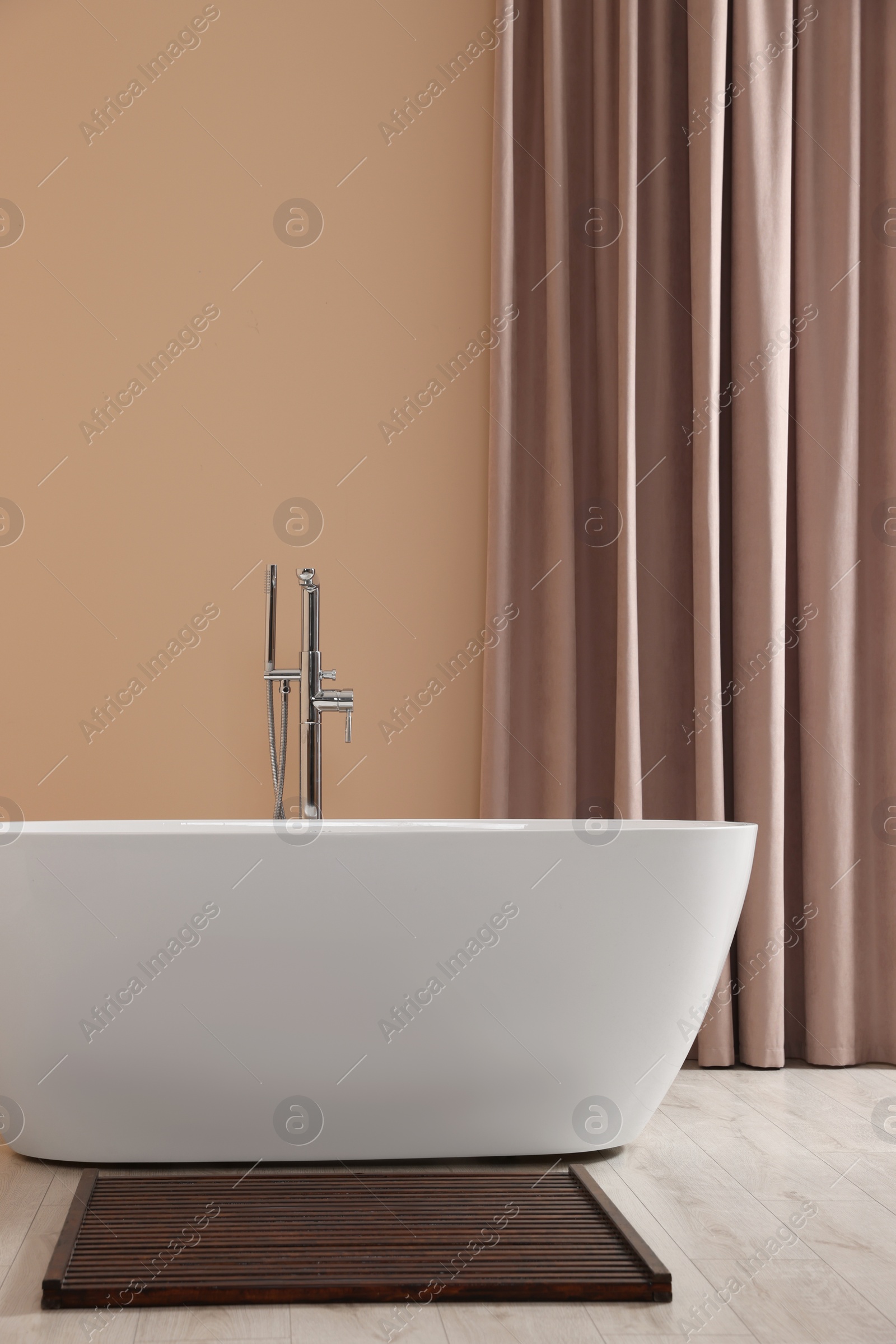 Photo of Stylish bathroom interior with ceramic tub near beige curtains